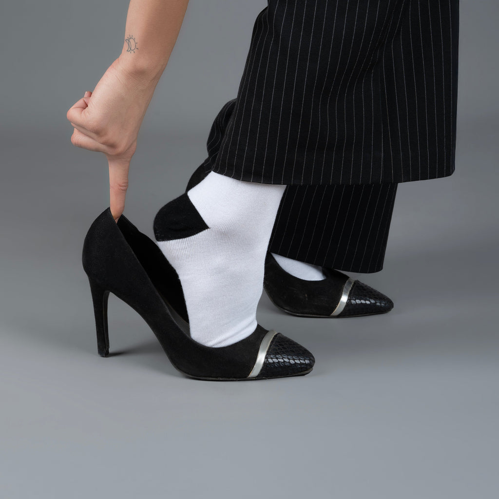 Person wearing black high-heeled shoes with white accents on a gray background