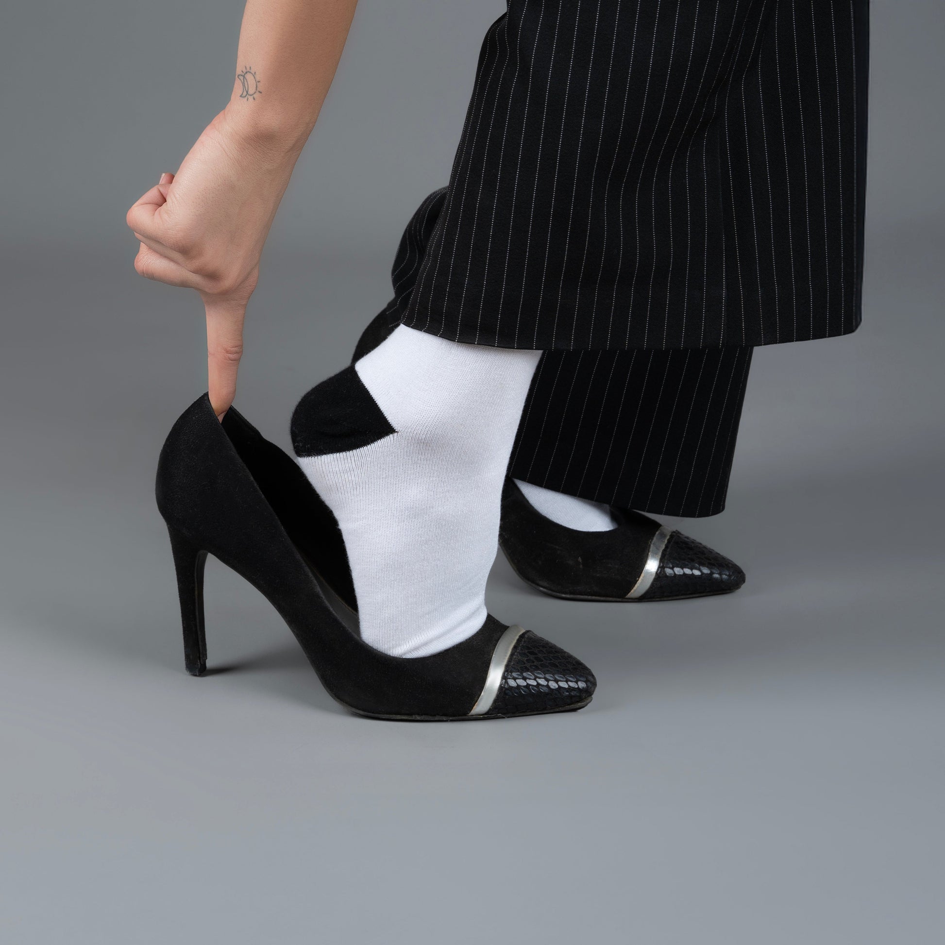 Person wearing black high-heeled shoes with white accents on a gray background