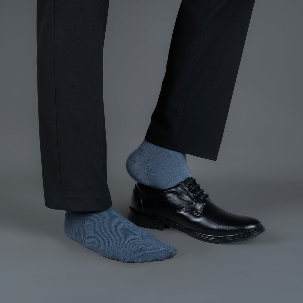 Person wearing black dress shoes and bamboo socks on a gray background