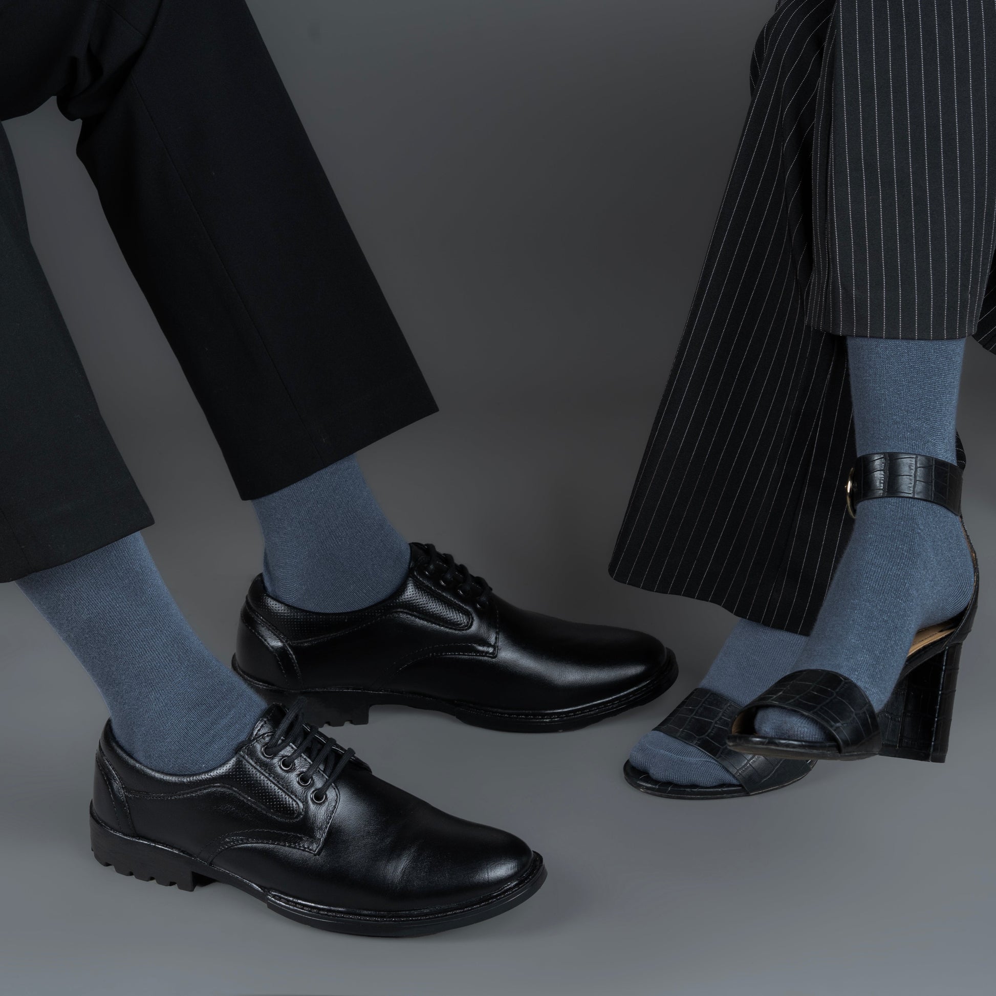 Two pairs of feet wearing black shoes and bombay gray bamboo socks against a gray background