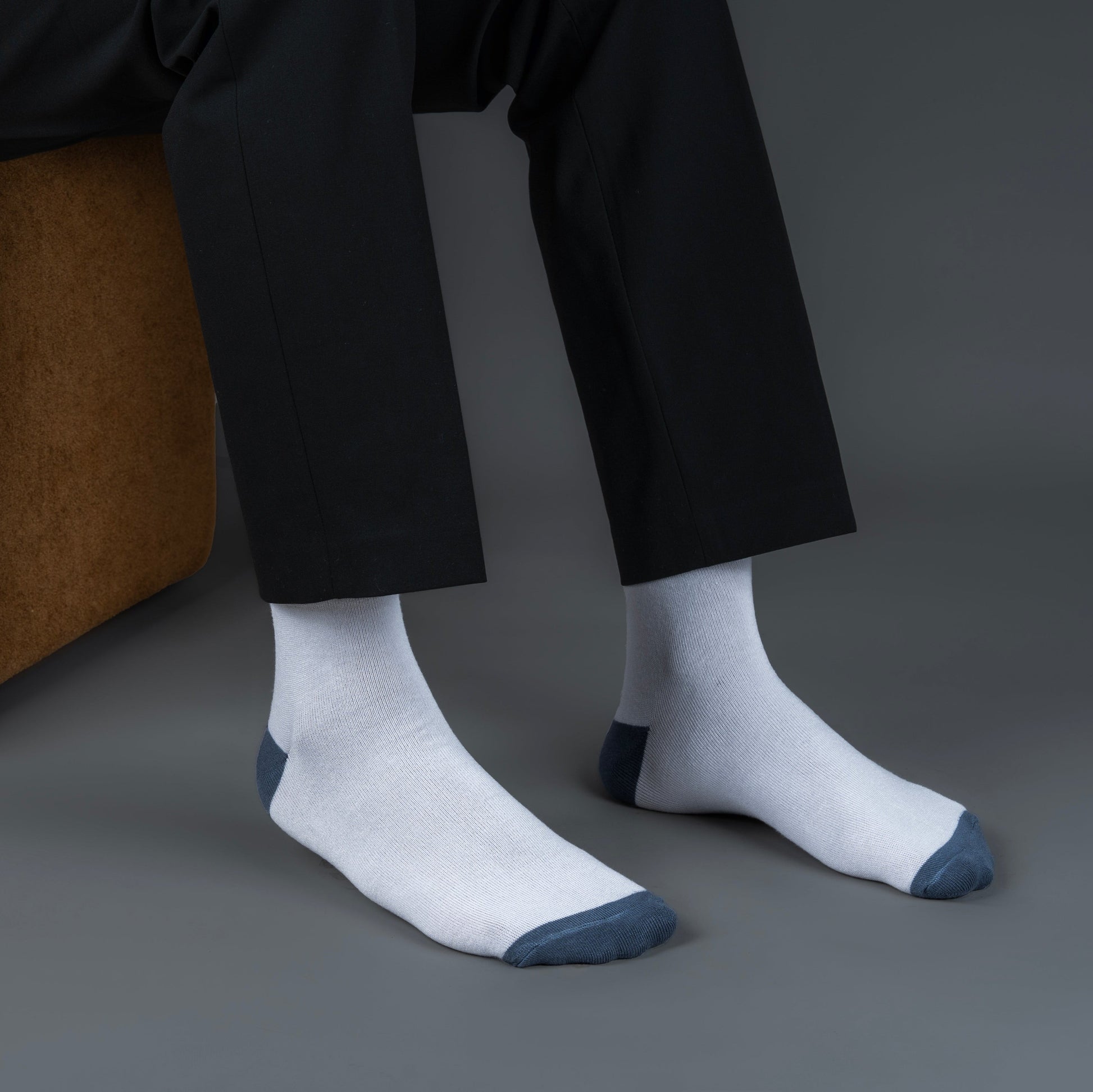 Person wearing white socks with toes and cuffs bamboo socks, sitting on a brown chair against a gray background.