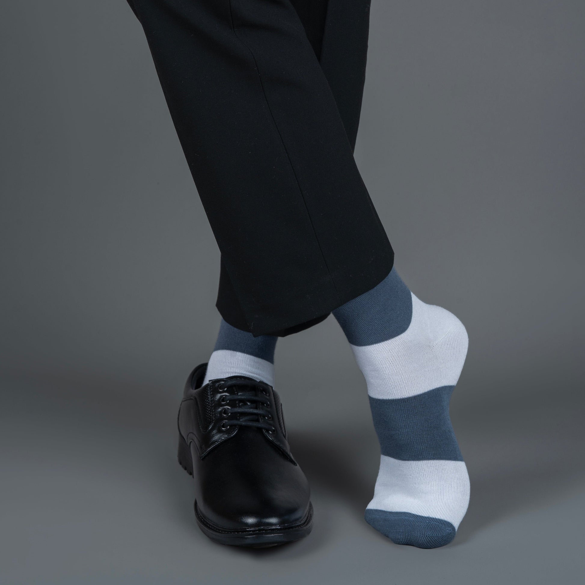 Person wearing black pants, black shoes, and bombay gray striped bamboo socks on a gray background