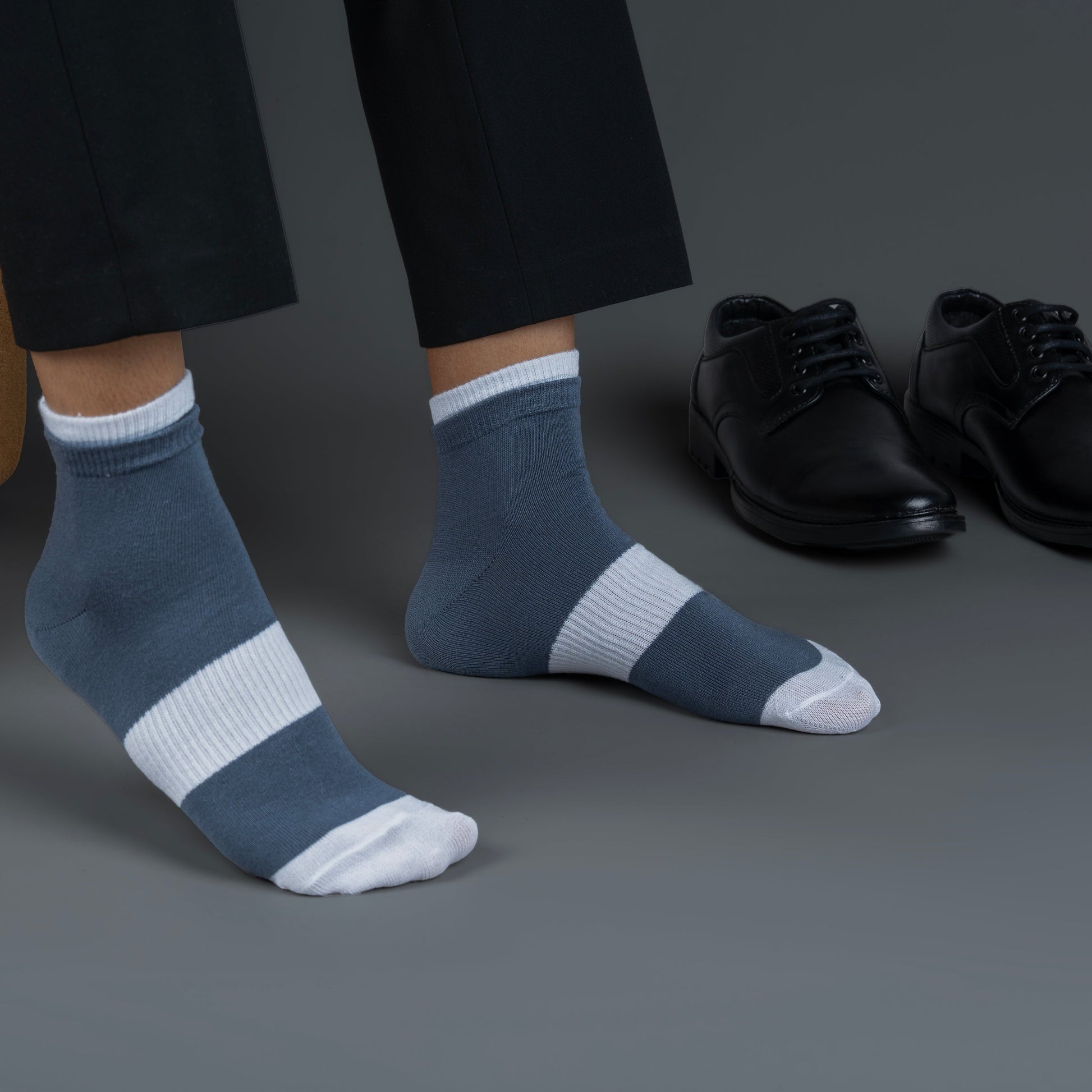 Person wearing blue bamboo socks with white stripes, standing next to a pair of black shoes on a gray background