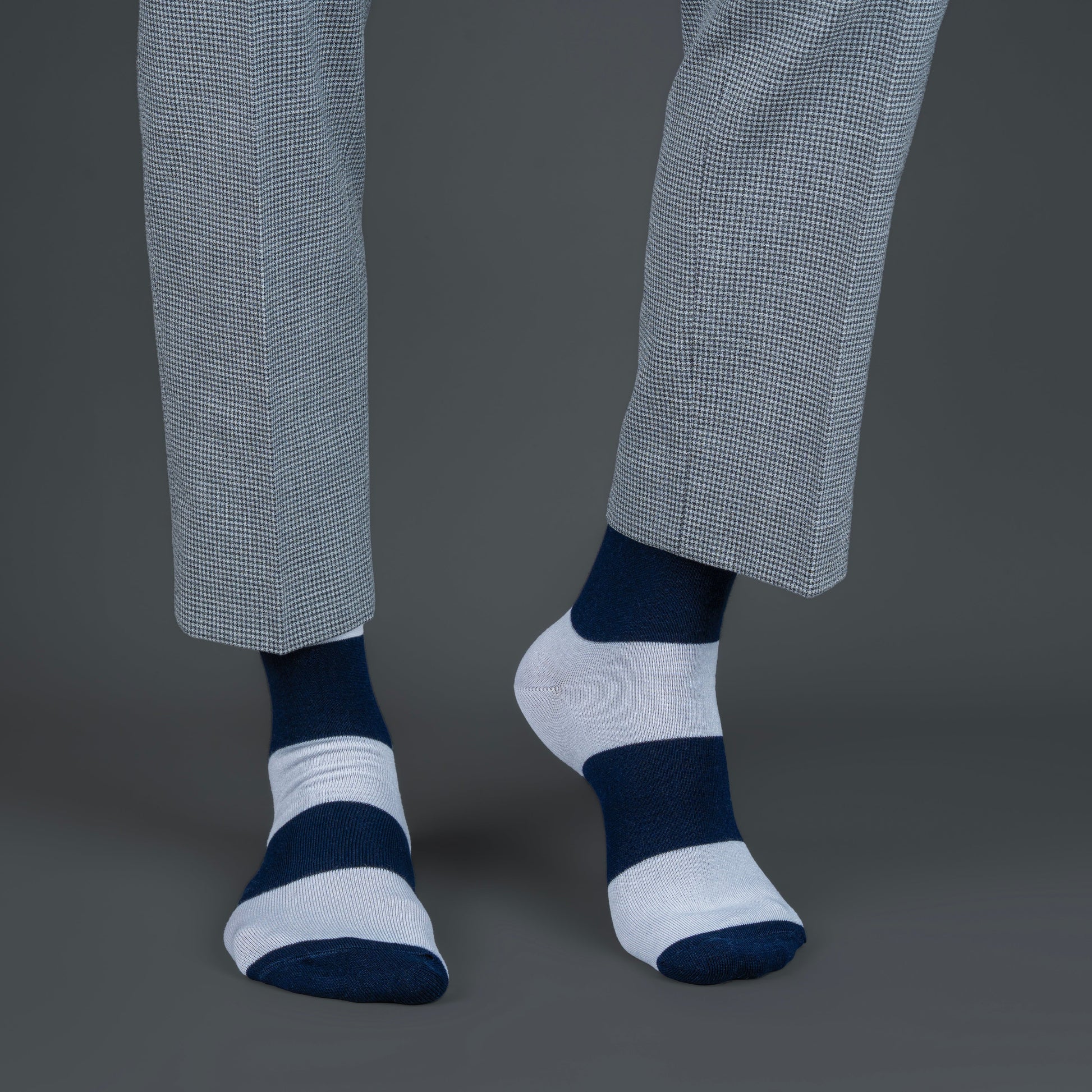 Person wearing gray pants and striped blue and white socks on a dark background