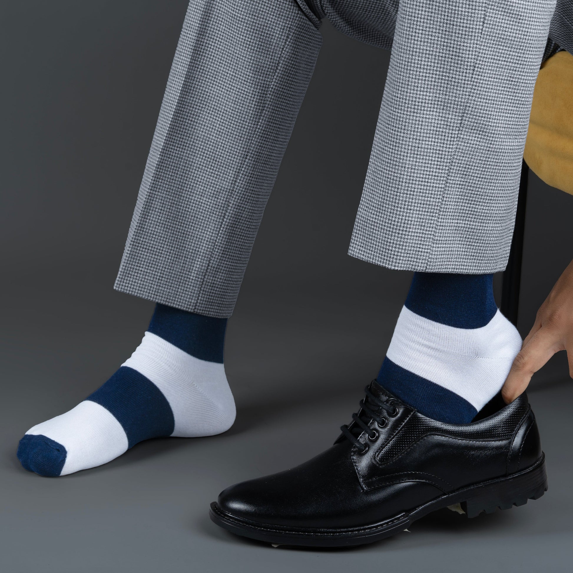 Person wearing navy and white striped socks with black dress shoes on a gray background