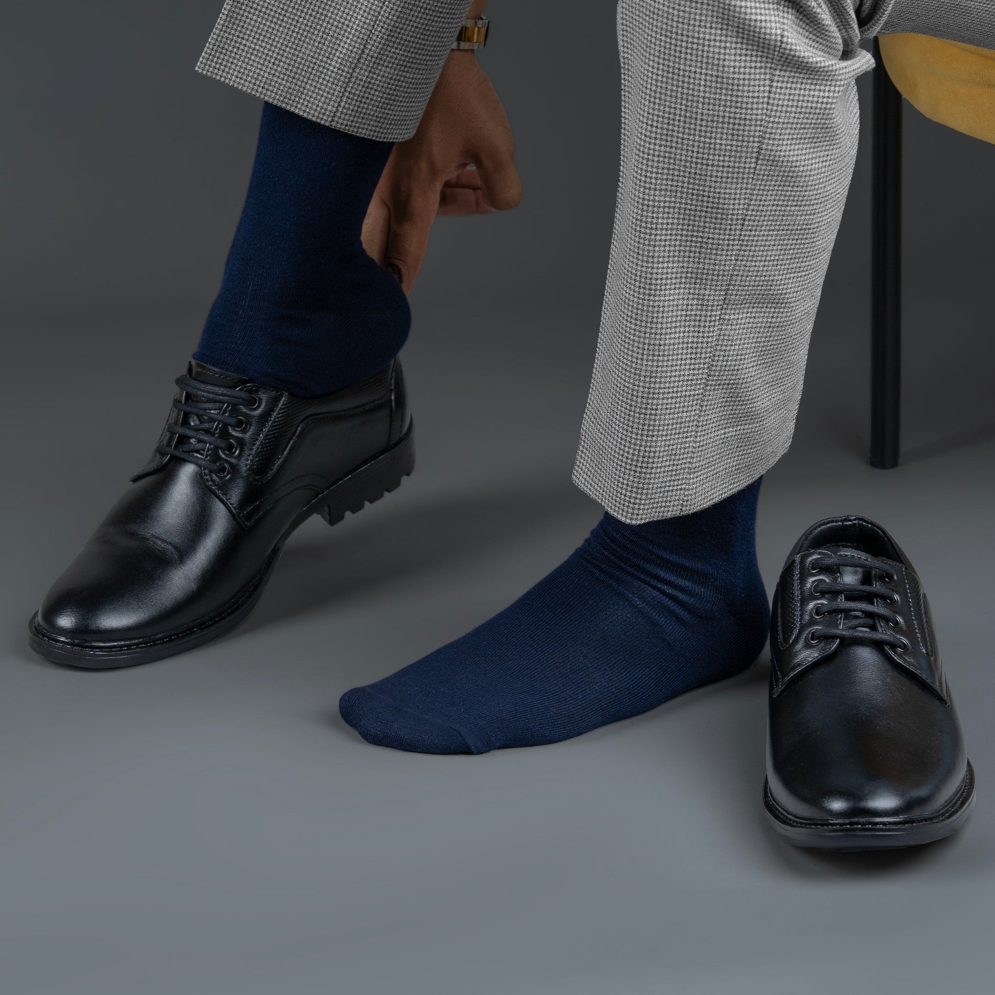 Person wearing black dress shoes and navy bamboo socks on a gray background