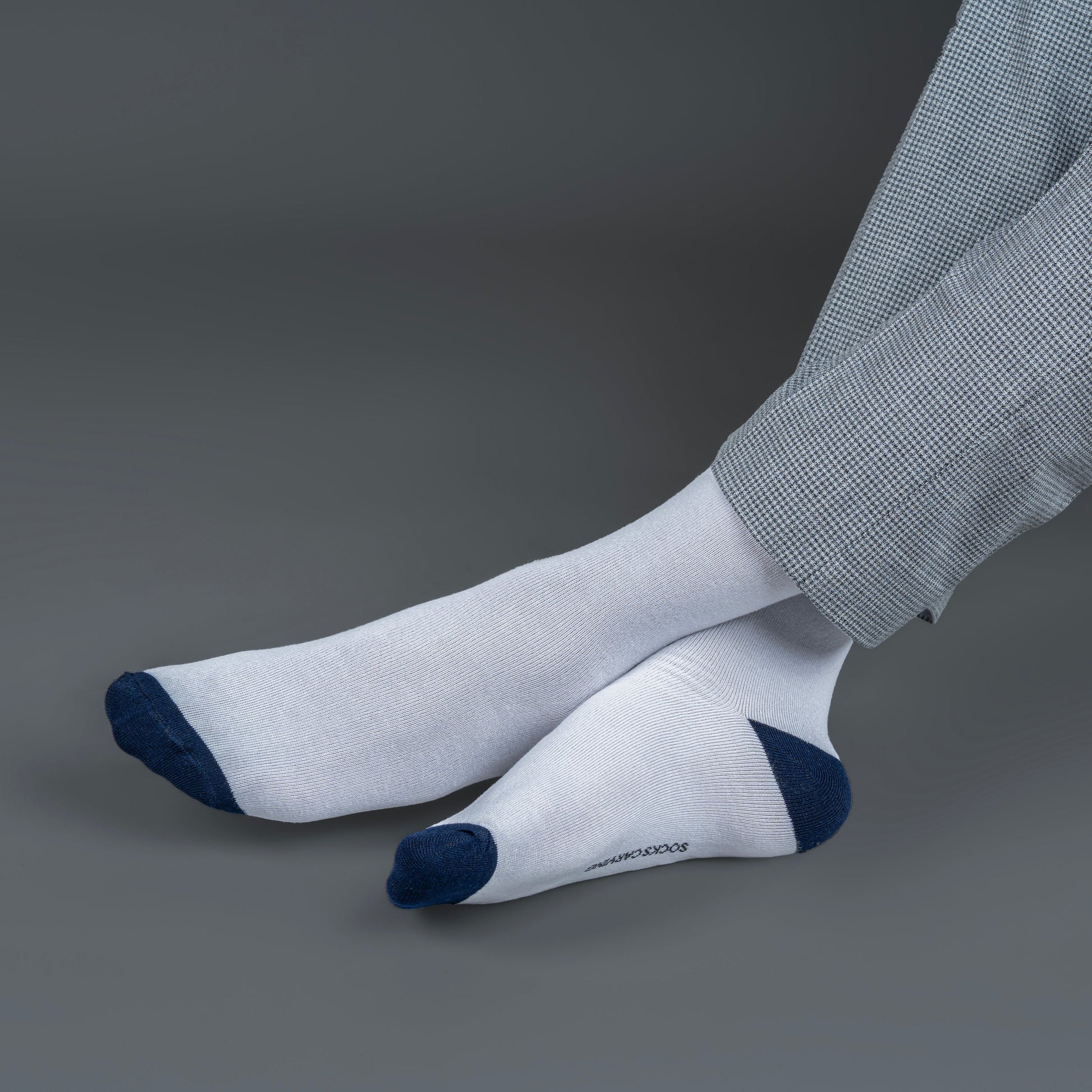 White socks with blue toes and cuffs worn with gray pants on a dark background