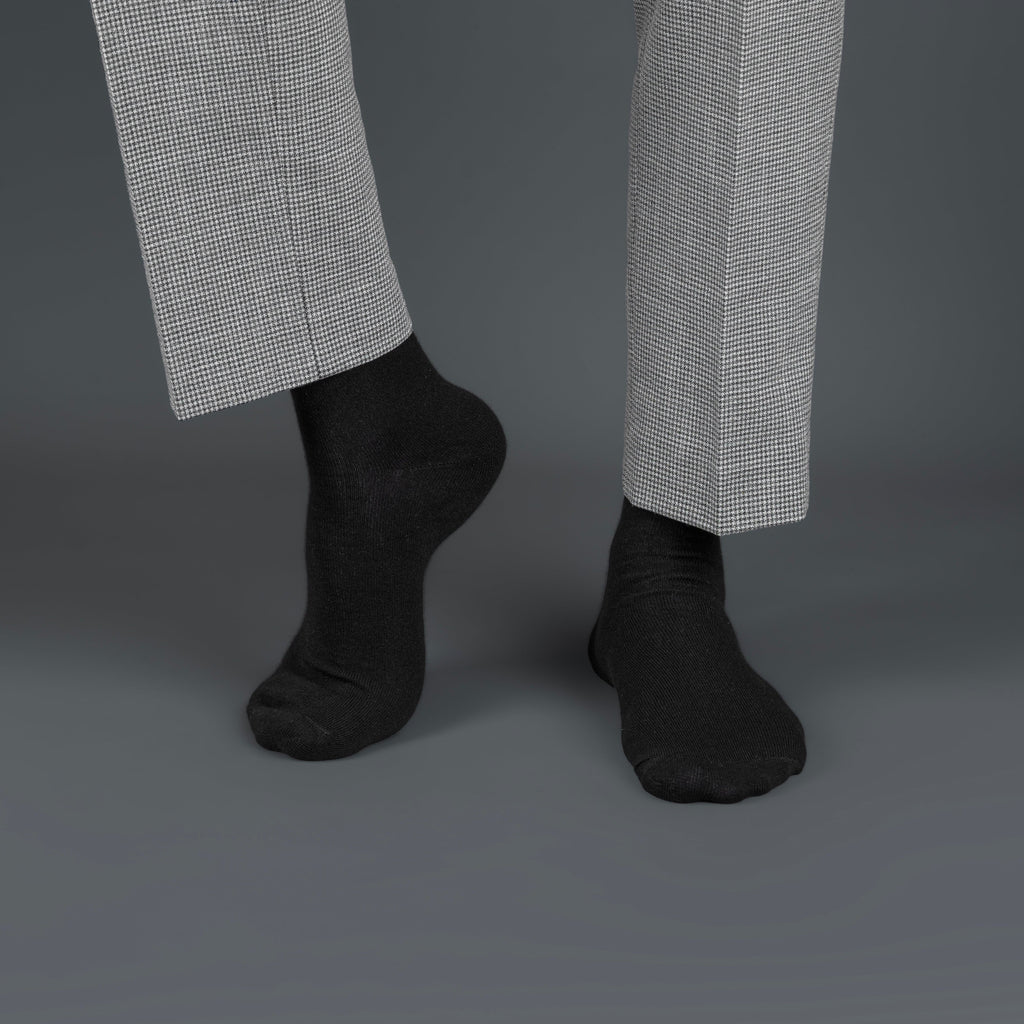 Black bamboo socks worn with gray checkered pants on a dark background