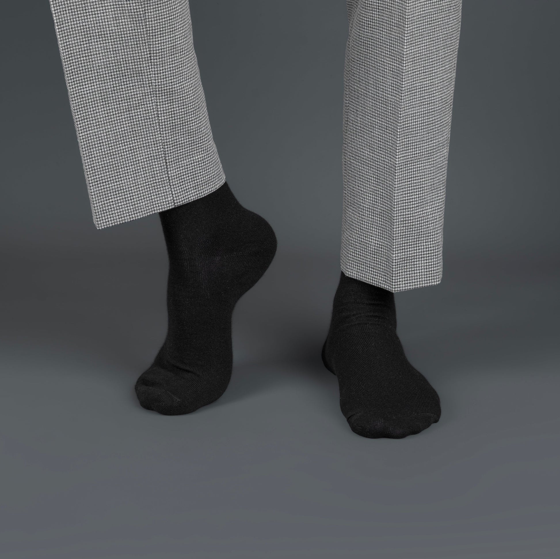 Black bamboo socks worn with gray checkered pants on a dark background