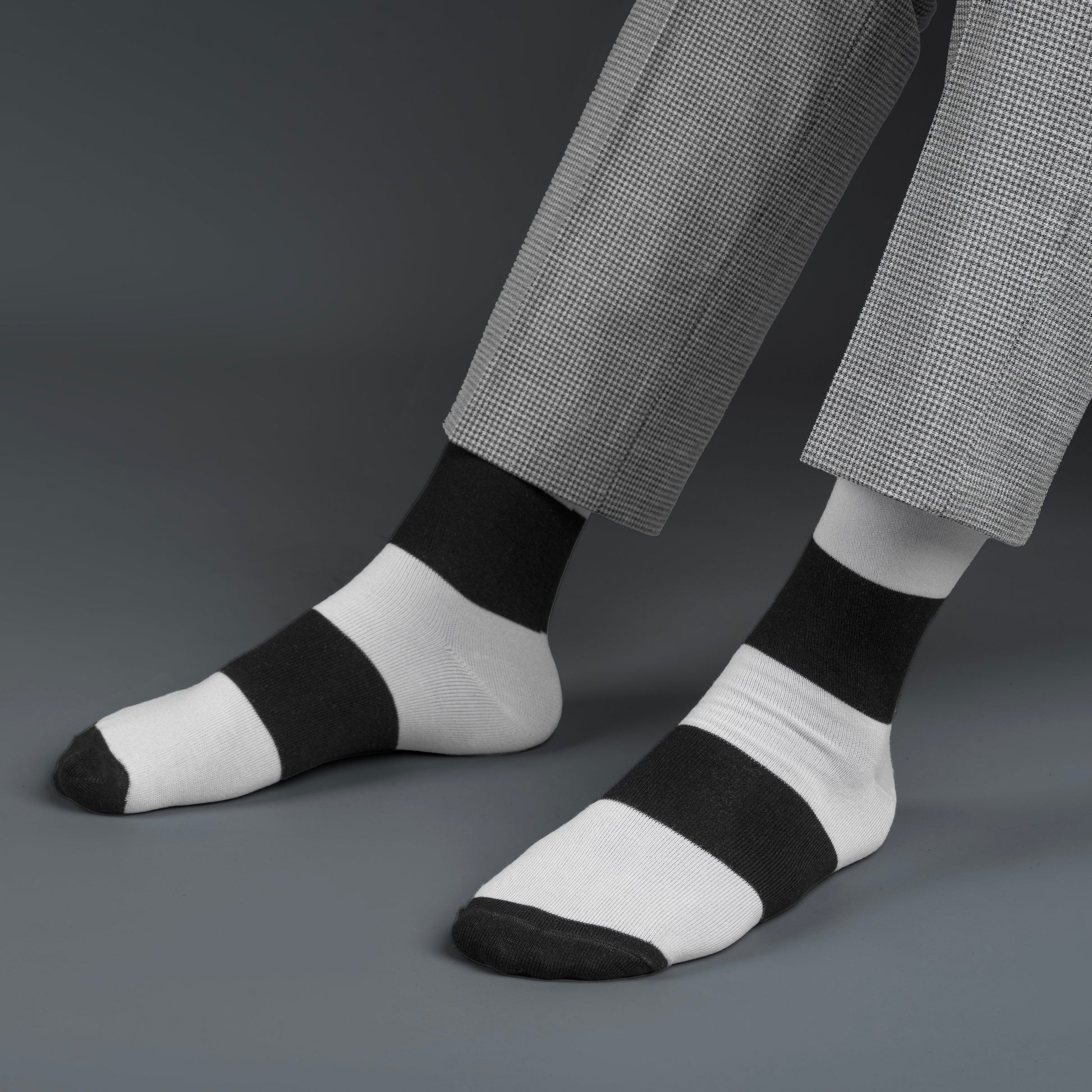 Black and white striped bamboo socks worn with gray pants on a dark background