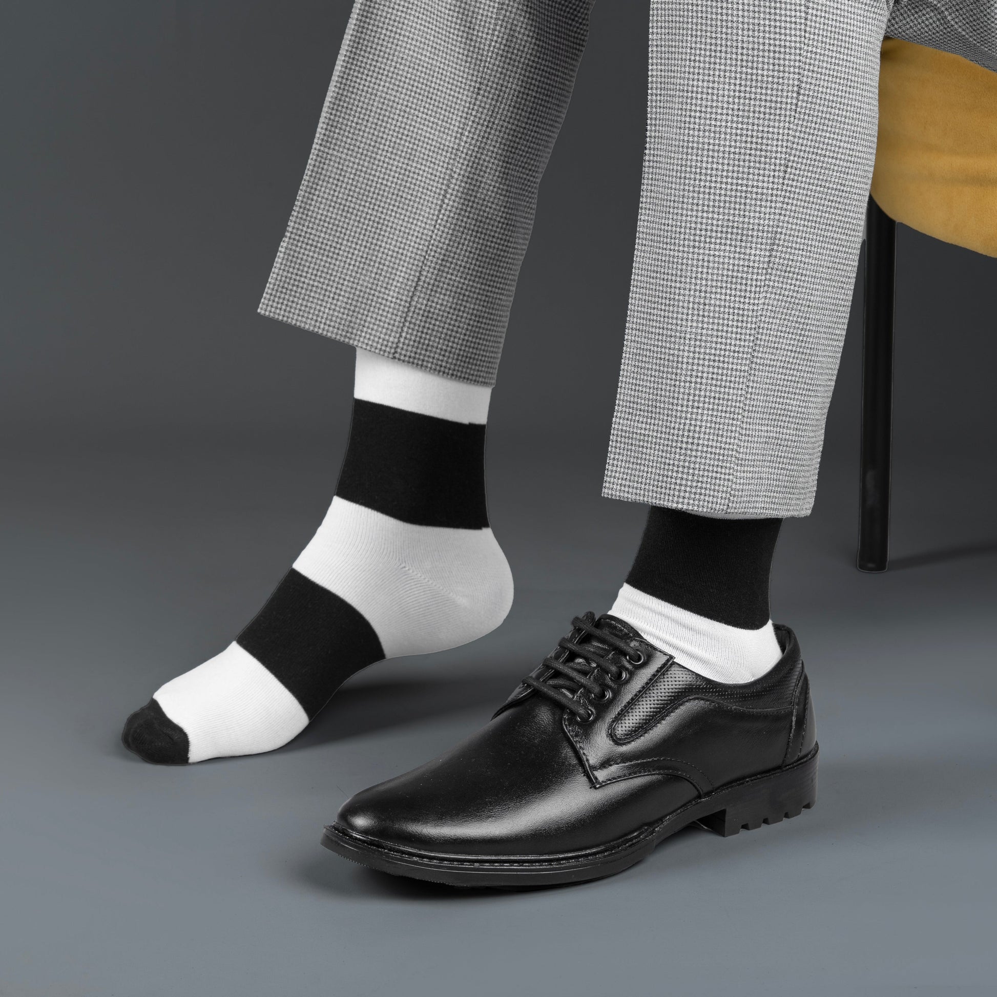 Person wearing black dress shoes, gray checkered pants, and black and white striped bamboo socks on a gray background.