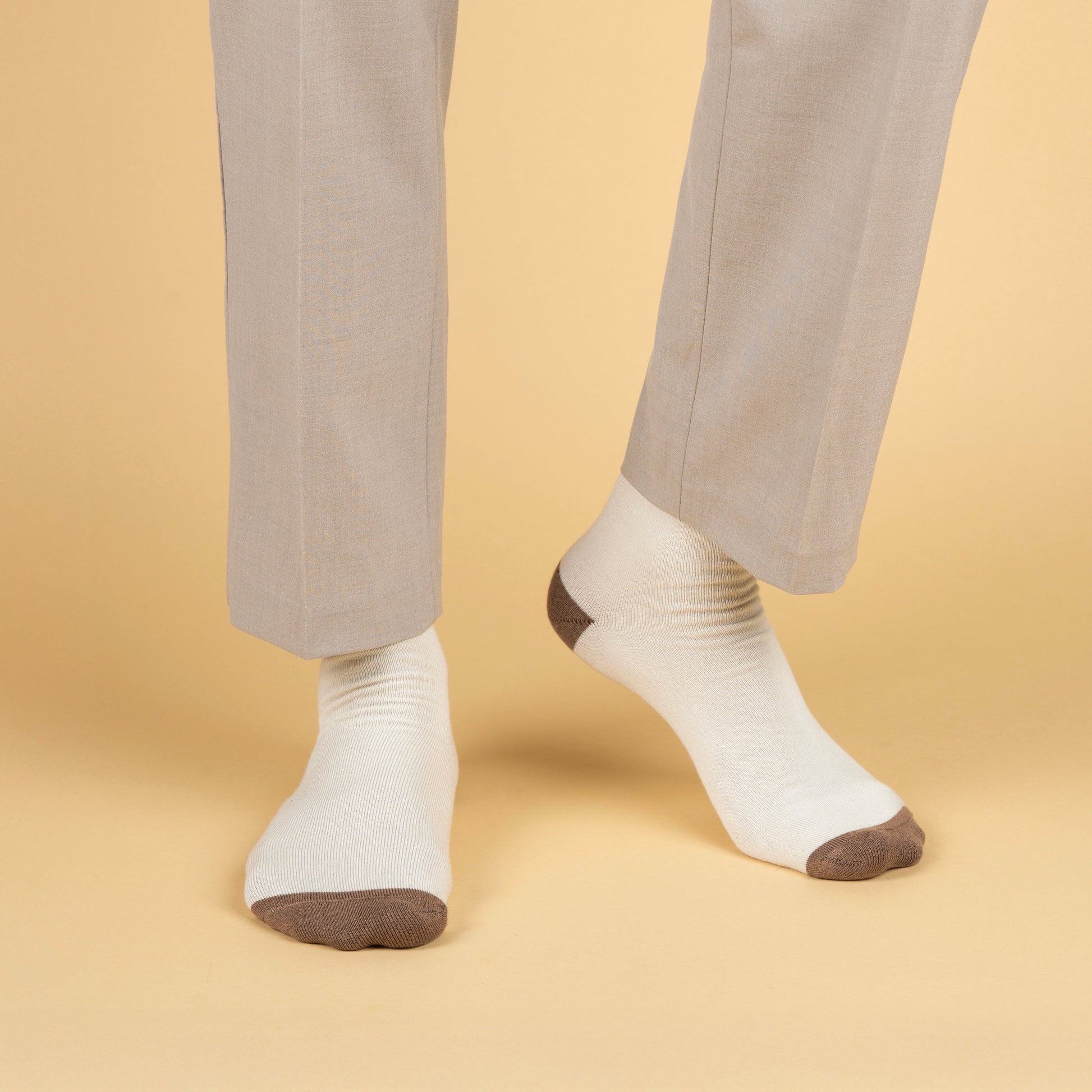 White socks with dark toes and heels worn with beige pants on a beige background