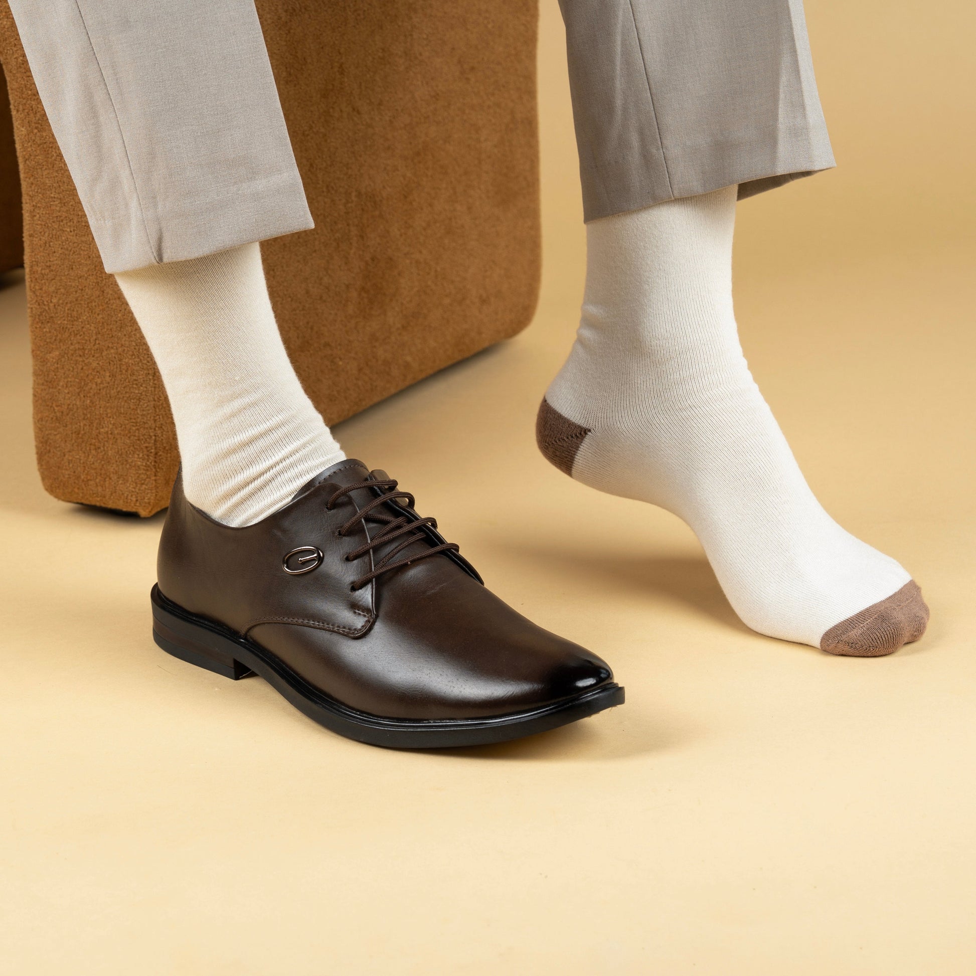 Brown leather shoes worn with white socks on a beige background