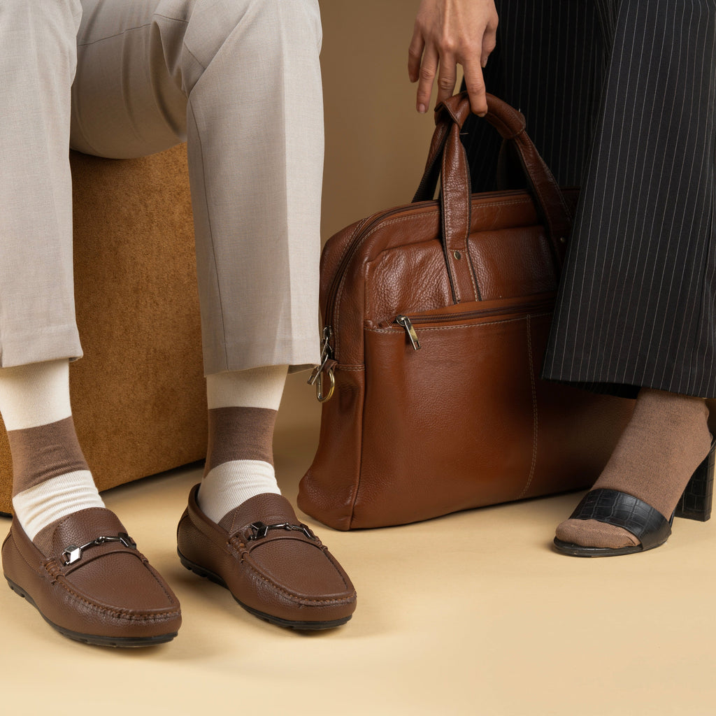 Two people sitting with a brown leather bag and brown bamboo socks on a beige floor.