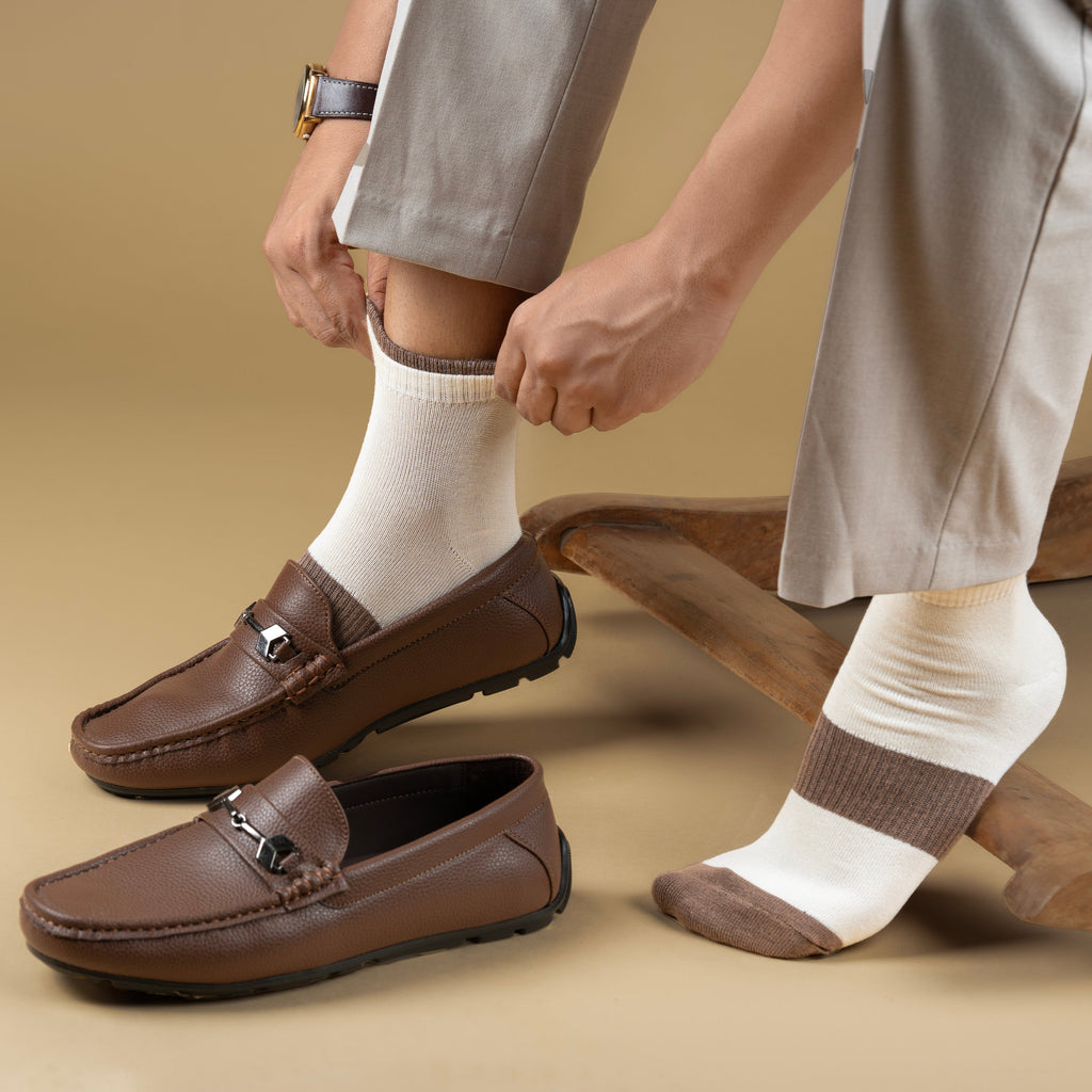 Brown loafers worn with white bamboo socks on a beige background