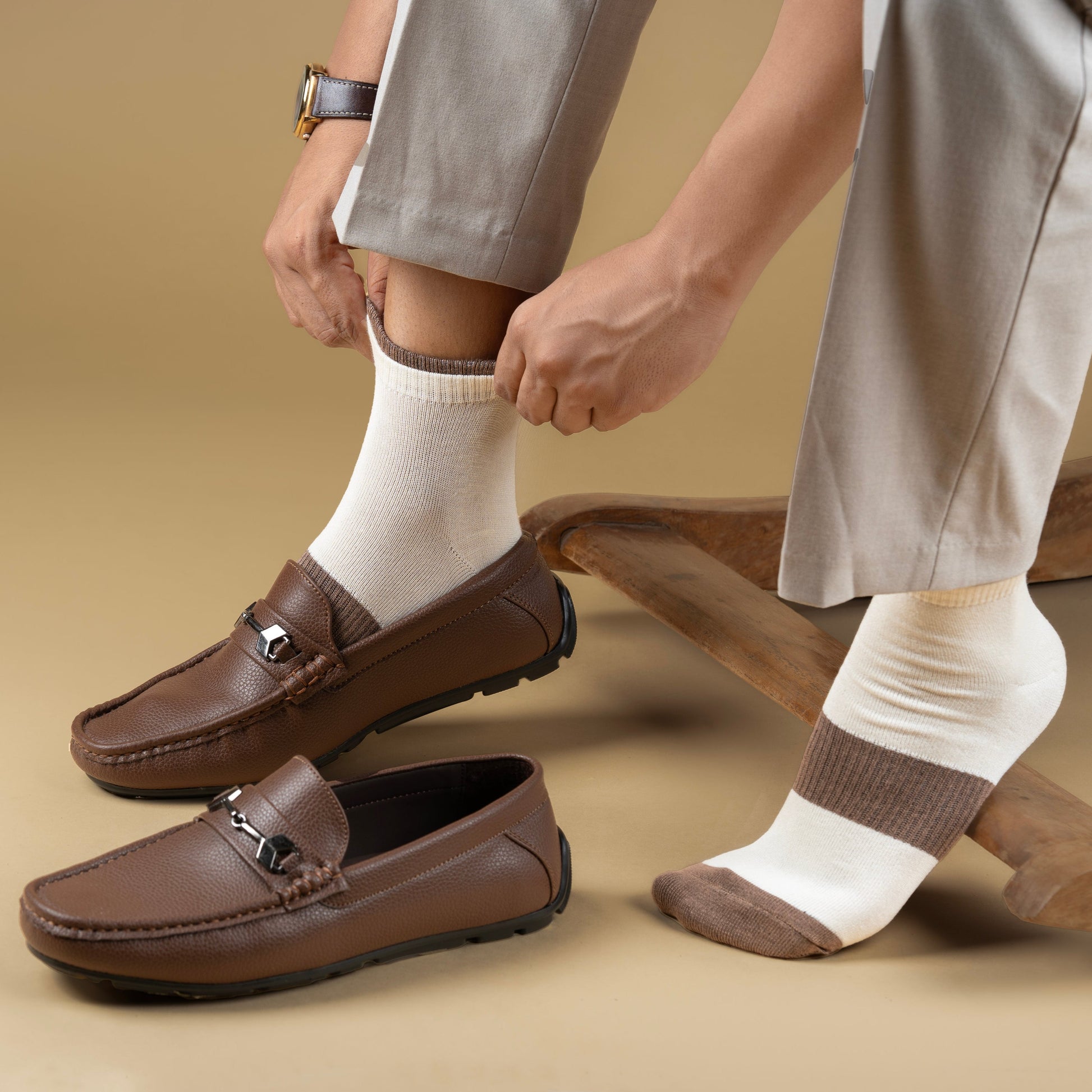 Brown loafers worn with white bamboo socks on a beige background