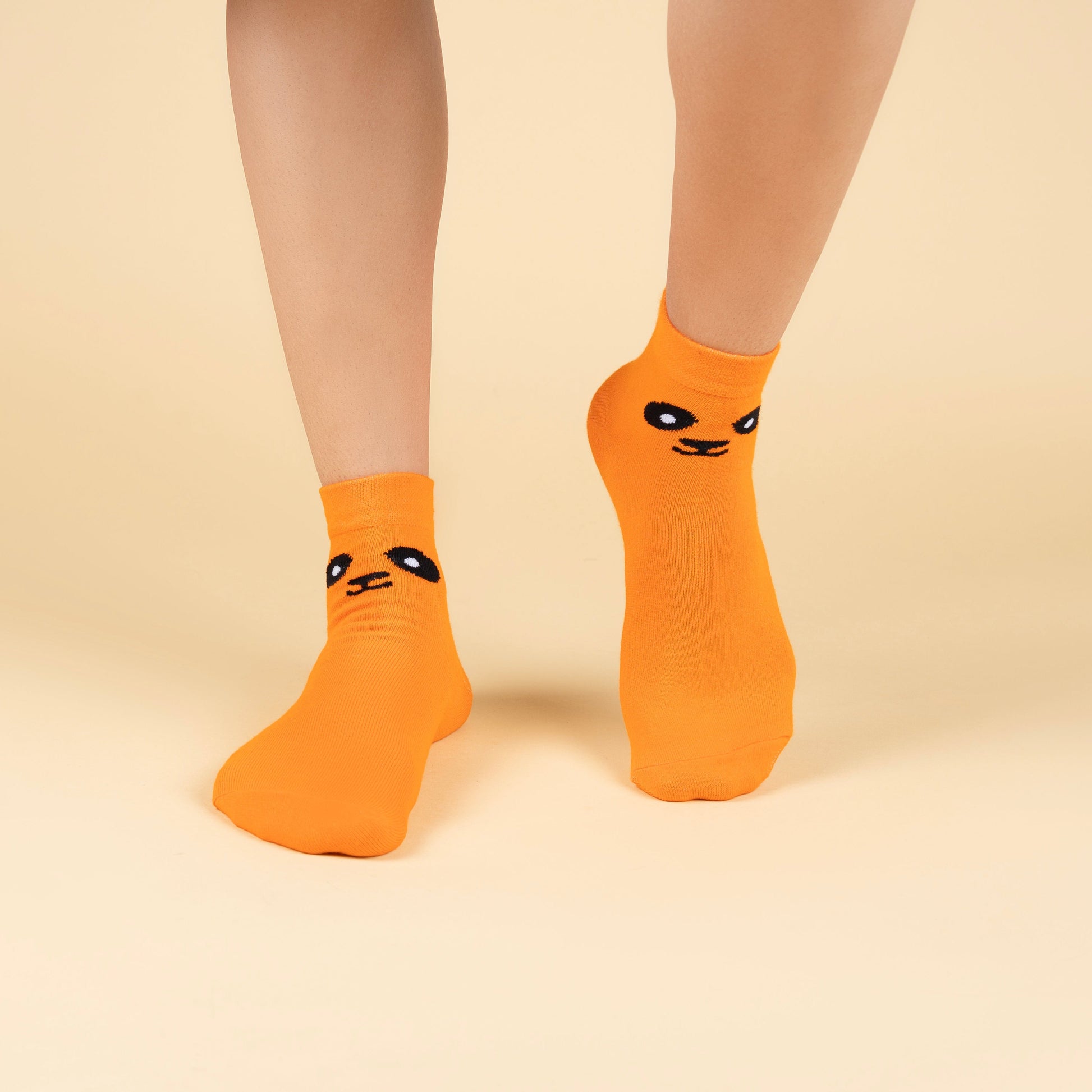 Orange socks with black smiley face design worn by a person on a beige background