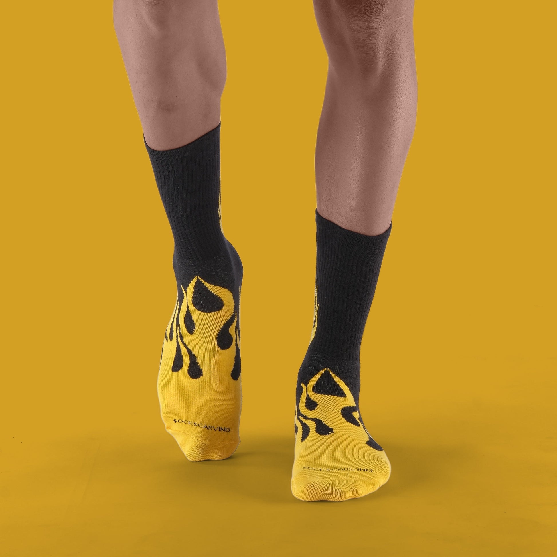 Person wearing black socks with yellow flame design on a mustard yellow background