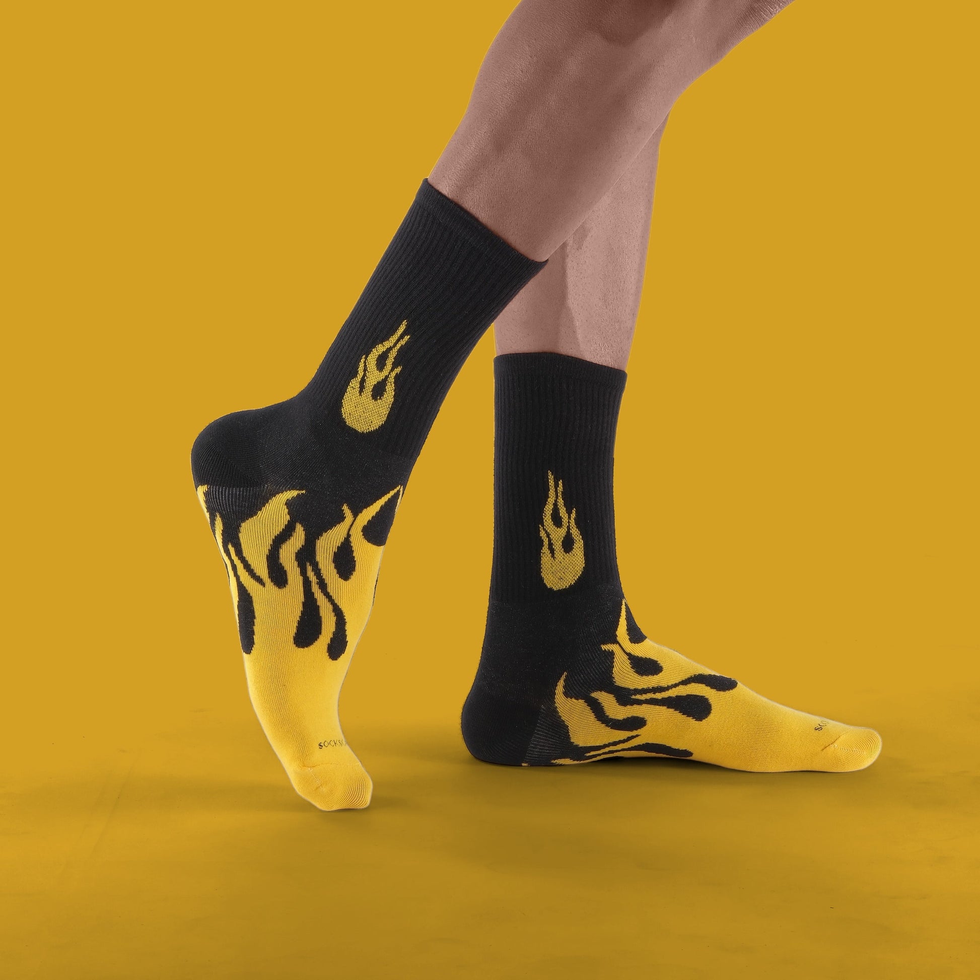 Person wearing black socks with yellow flame designs on a mustard yellow background
